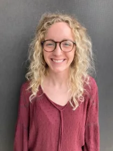 Headshot of Hannah GIll. Hannah is a white woman with blond curly hair. She is wearing a pink blouse and glasses.