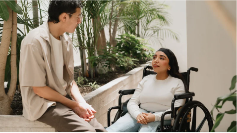 A woman and man talk with each other. The woman is using a wheelchair.