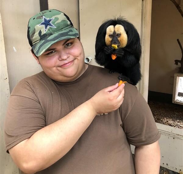 Matthew Leos smiles and feeds a small monkey sitting on his shoulder.