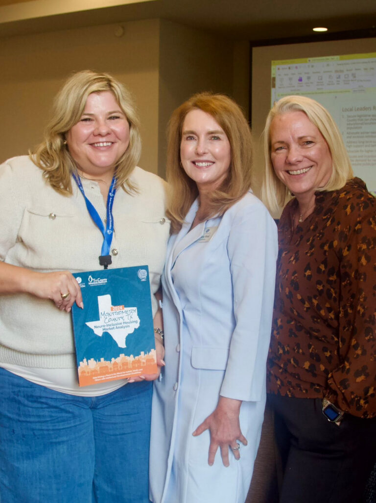 A group of three Council members and Council meeting participants standing together. One holds up a printed report with an outline of Texas on the cover.